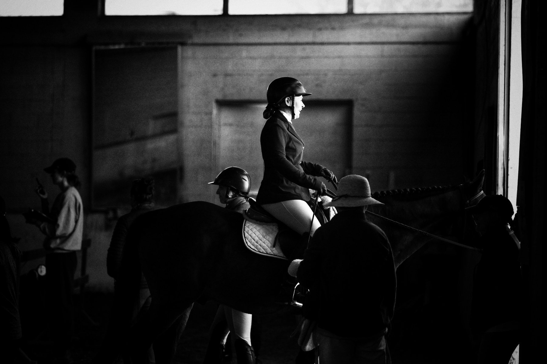 A rider in the indoor school, the rail in shadow