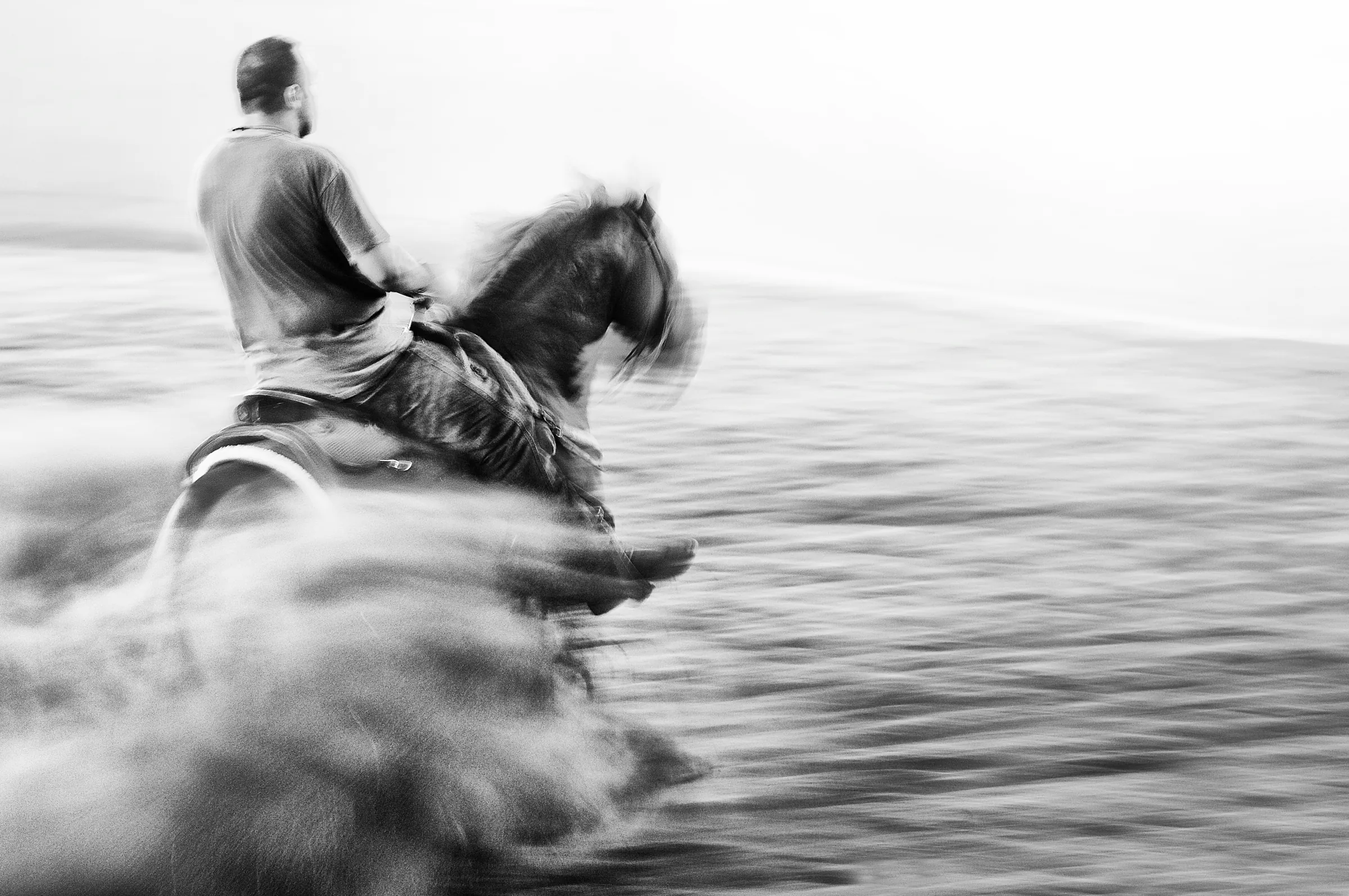 A rider at speed through the surf, in black and white